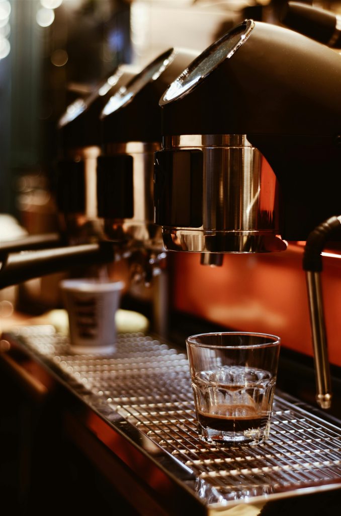 A fresh shot of espresso pours into a glass from a sleek coffee machine in a cozy cafe.